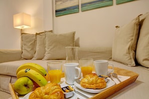 A breakfast tray with croissants, bananas, juice, and coffee on a bed with pillows and a lamp. - Apartment 'Little Gem' in a Central Location with Wi-Fi (Cruce de Arinaga)