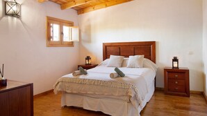 A bedroom with a wooden bed, two bedside tables, a nightstand, a window, and a wall-mounted light fixture. - Country House 'Casa Rural Los Colorados' with Mountain Views and Pool (Vega de San Mateo)