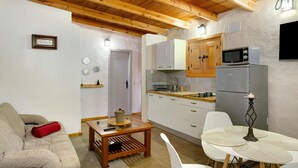 A compact living space with a sofa, a small table, a kitchen area with cabinets and appliances, and a dining table with placemats. - Country House 'Casa Rural Los Colorados' with Mountain Views and Pool (Vega de San Mateo)