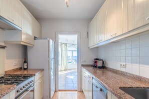 Una cocina con armarios blancos, estufa, refrigerador y ventana que da a un balcón.