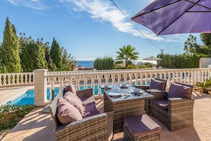An outdoor dining area with wicker furniture, a pool, and a view of the sea.