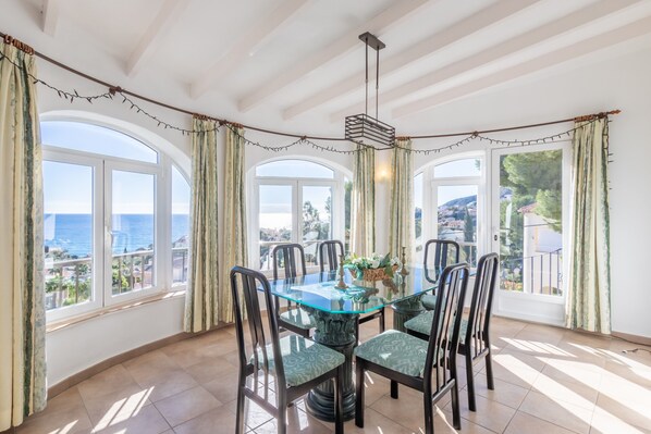 A dining area with a glass table, chairs, and a view of the sea.