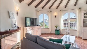 Uma sala de estar com sofá, televisão, lareira e vista para o exterior.