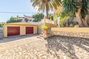 A building with two red doors, a stone wall, and a palm tree.