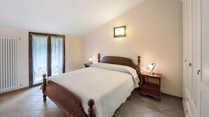 A bedroom with a wooden bed, a nightstand, a lamp, a radiator, and a sliding glass door. - Pet Friendly Apartment 'Messalina Agriturismo La Scuderia' with Wi-Fi (Andora)