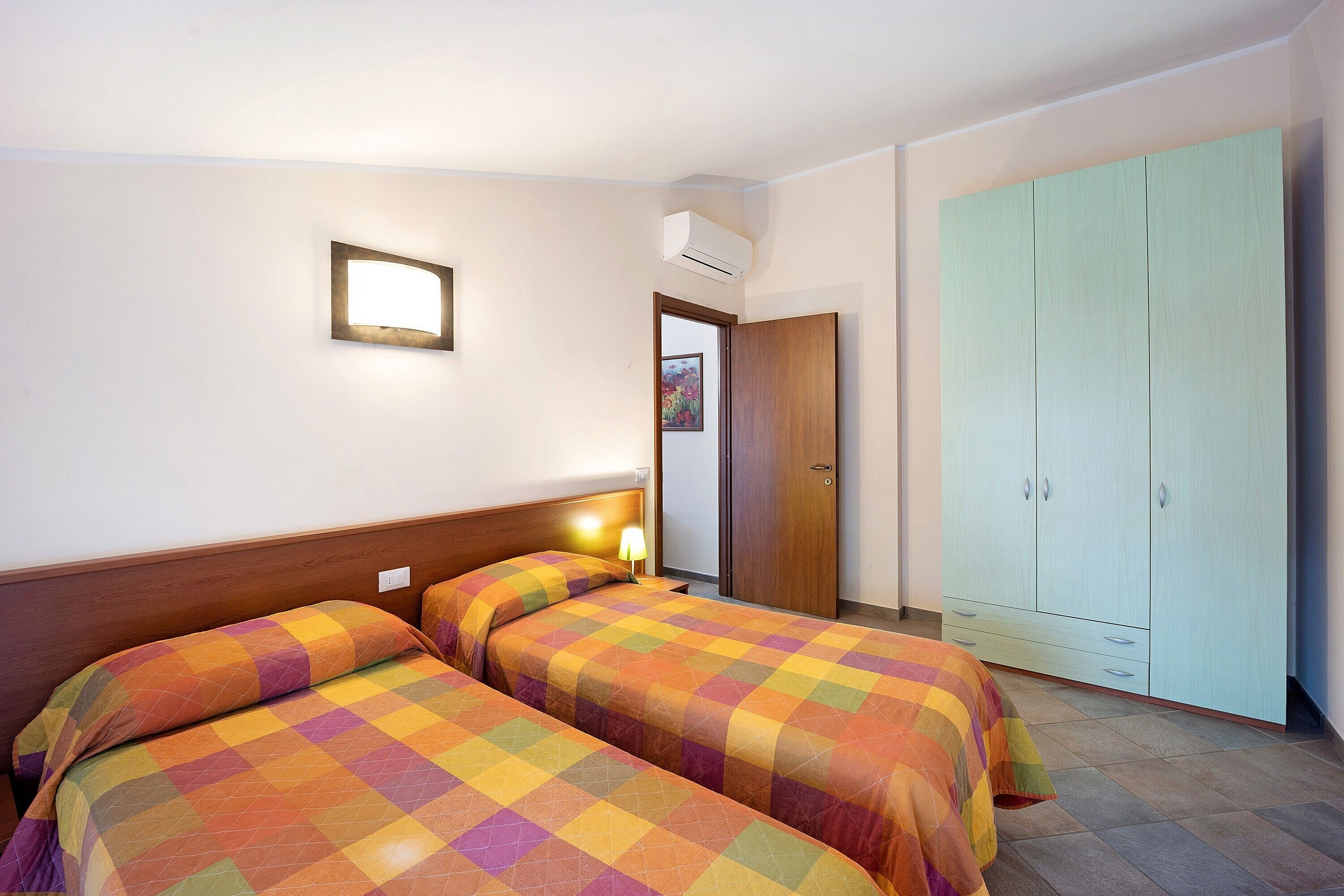 Une chambre avec deux lits, une armoire et un climatiseur fixé au mur.
