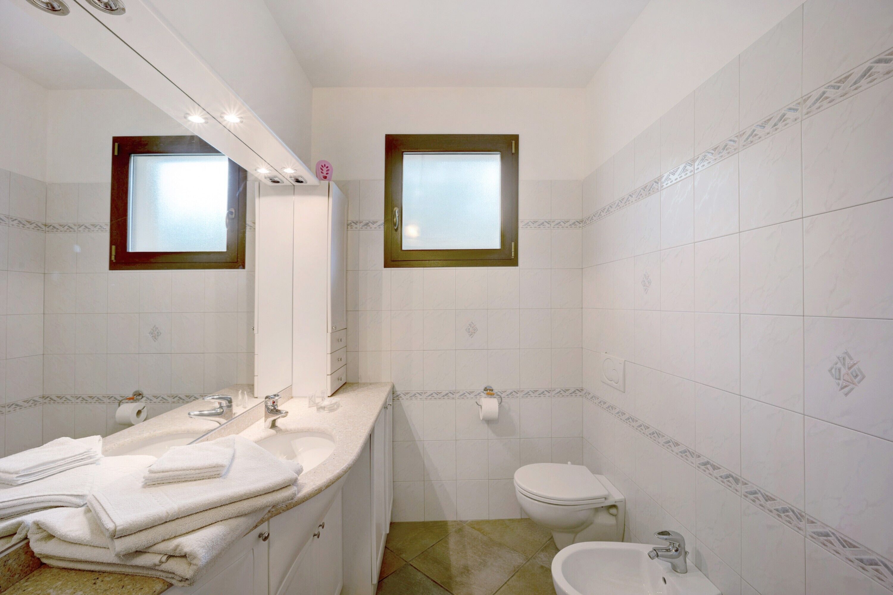 A bathroom with a sink, mirror, toilet, and a window.