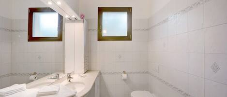 A bathroom with a sink, mirror, toilet, and a window.