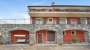A two-story building with a stone facade, a balcony with metal railings, and a swing seat in front.