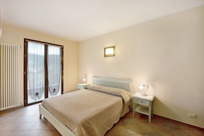 Une chambre à coucher comprenant un lit, des tables de chevet, une commode, une fenêtre avec des rideaux et un luminaire fixé au mur.
