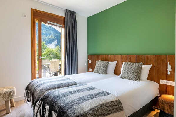 Quarto com cama grande, cabeceira de madeira, vista para o verde lá fora e janela com cortinas.