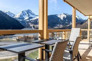 A wooden deck with tables and chairs overlooking snow-capped mountains. - Chalet in French Alps with Mountain Views (Abondance)