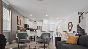 A modern living room with a gray sofa, a coffee table, and a dining area with chairs and a kitchen in the background. - Harry Potter, Frozen & Pool Fun Near Disney (Kissimmee)