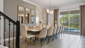A dining area with a long table, chairs, a chandelier, and a view of a swimming pool. - Harry Potter, Frozen & Pool Fun Near Disney (Kissimmee)