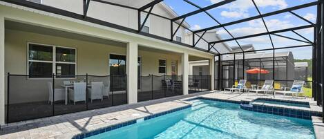 A swimming pool with a glass enclosure, a covered patio area with seating, and a view of the sky.
