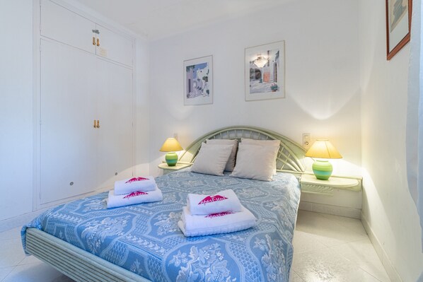 Una cama bien hecha con ropa de cama estampada, dos lámparas de noche y dos cuadros en la pared.