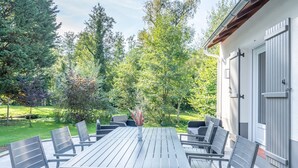 An outdoor patio with a wooden table and chairs, surrounded by greenery and trees. - Fully self-contained cottage (Inxent)