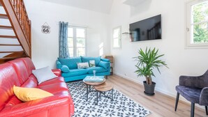 A living room with a red leather sofa, a blue sofa, a wooden coffee table, a patterned rug, a potted plant, and a TV mounted on the wall. - Fully self-contained cottage (Inxent)