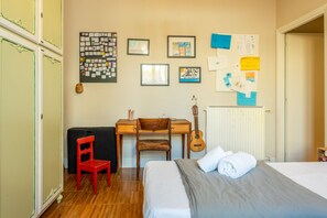 Un dormitorio con cama, escritorio, silla, guitarra y radiador.