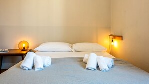Ein Hotelzimmer mit einem Bett, zwei Kissen, einem Nachttisch mit Lampe und gerollten Handtüchern.