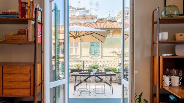 Eine offene Tür, die zu einer Terrasse mit Tisch und Stühlen führt, umgeben von Bücherregalen und einem Schrank.