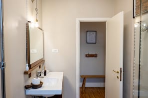 A bathroom with a white sink, a mirror, a framed picture on the wall, and a wooden shelf.