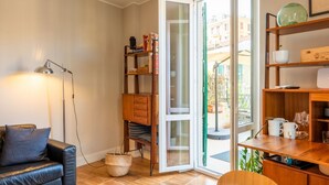 Ein gemütliches Wohnzimmer mit einer Ledersofa, einer Stehlampe, einem Holzregal und einem Essbereich mit Tisch und Stühlen.