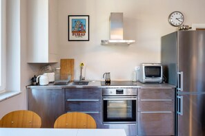 A modern kitchen with stainless steel appliances, a clock, and a framed picture on the wall.