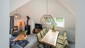 Ein modernes Loft mit hohen Decken, einem Essbereich mit einem Holztisch und grünen Sitzmöbeln, einem Kamin und Pendelleuchten.