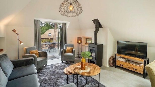 Ein modernes Wohnzimmer mit einer Couch, Sesseln, einem Fernseher, einem Kamin und einem großen Fenster.