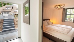 Ein Schlafzimmer mit Bett, Nachttisch, Wandlampe und einem Fenster mit Vorhängen.