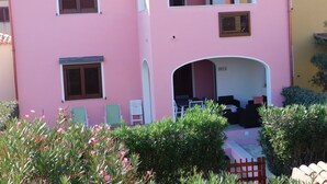 Ein pinkfarbenes Gebäude mit zwei Balkonen, einem überdachten Eingangsbereich und einem kleinen Garten.