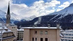 Un edificio con una torre de reloj, rodeado de montañas nevadas y un cielo despejado.