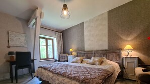 Ein Schlafzimmer mit einem großen Bett, einem Sessel, einem Schreibtisch und einem Fenster.