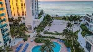 A resort with a pool surrounded by lounge chairs, palm trees, and a view of the ocean. - Great apartment in Hollywood with side ocean view! Direct exit to the beach! (Hollywood)