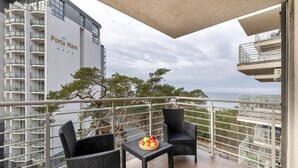 Ein Balkon mit Korbstühlen und einem Tisch mit Früchten, Blick auf ein Gebäude mit der Aufschrift 'Porta Mare' und eine Meeransicht.