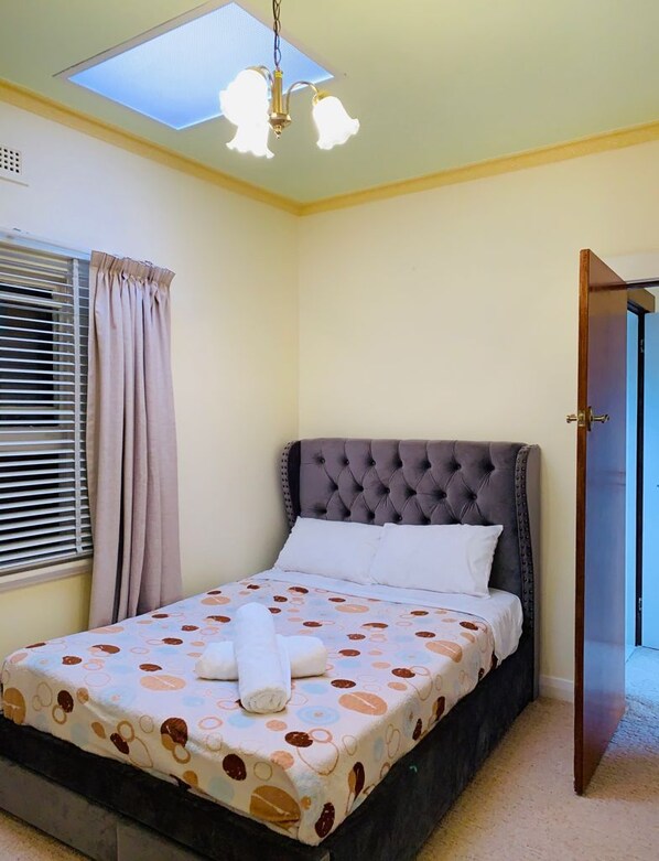 A bedroom with a bed, a window with curtains, a door, and a skylight.