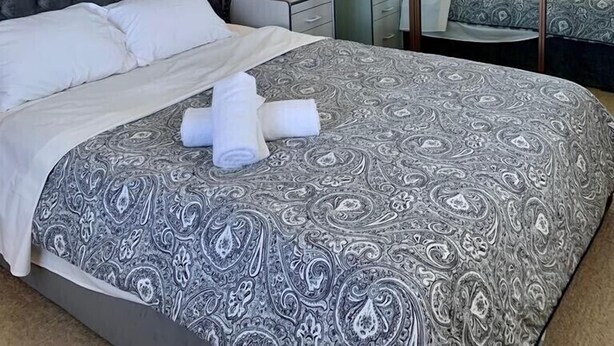 A hotel room with a large bed, a nightstand with a lamp, a mirror, and a ceiling fan. - Beautiful scenery in Glenorchy with mountain and water view (Glenorchy)
