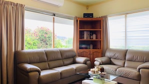 A living room with two beige leather sofas, a glass coffee table, and a wooden cabinet with shelves. - Beautiful scenery in Glenorchy with mountain and water view (Glenorchy)