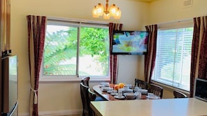 A kitchen with a central island, wooden cabinets, a dining table with chairs, a refrigerator, and a TV mounted on the wall. - Beautiful scenery in Glenorchy with mountain and water view (Glenorchy)