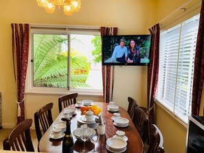 A dining area with a table set for four, a television mounted on the wall, and a window with curtains.