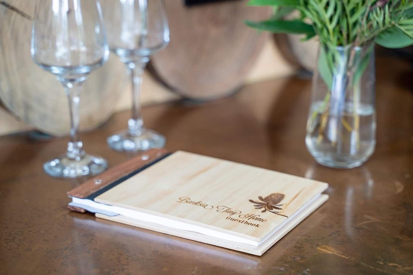Ein Gästebuch aus Holz mit der Aufschrift "Parkside Jump Home guest book" auf einem Tisch mit Weingläsern und einem Blumenstrauß.