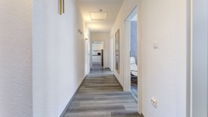 A hallway with a wooden floor, white walls, and a door leading to a bathroom. - Haus Nr. 9 (Wolgast)