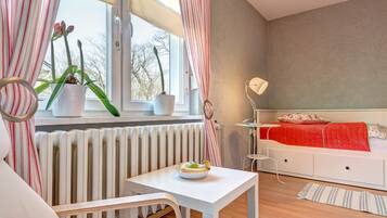 A modern bedroom with a white bed, a red blanket, and a window with striped curtains.