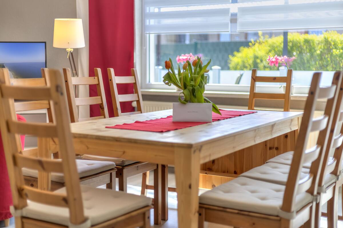 A dining area with a wooden table and chairs, a vase of flowers, and a lamp.