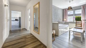 A modern apartment with a wooden floor hallway, a dining area with a white table and chair, and a kitchen in the background. - Haus Nr. 9 (Wolgast)