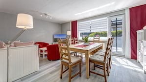 A modern dining area with a wooden table and chairs, a red sofa, and a white radiator. - Haus Nr. 9 (Wolgast)