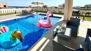 Une piscine avec des jeux gonflables, du mobilier d’extérieur et une vue sur la mer.