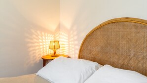 A bed with white linens, a wicker headboard, and a small bedside table with a lamp casting a warm glow. - Siracusa Horizon Home by Wonderful Italy (Siracusa)