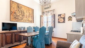 A living room with a wooden cabinet, a television, a dining table with blue chairs, and a large painting on the wall. - Siracusa Horizon Home by Wonderful Italy (Siracusa)